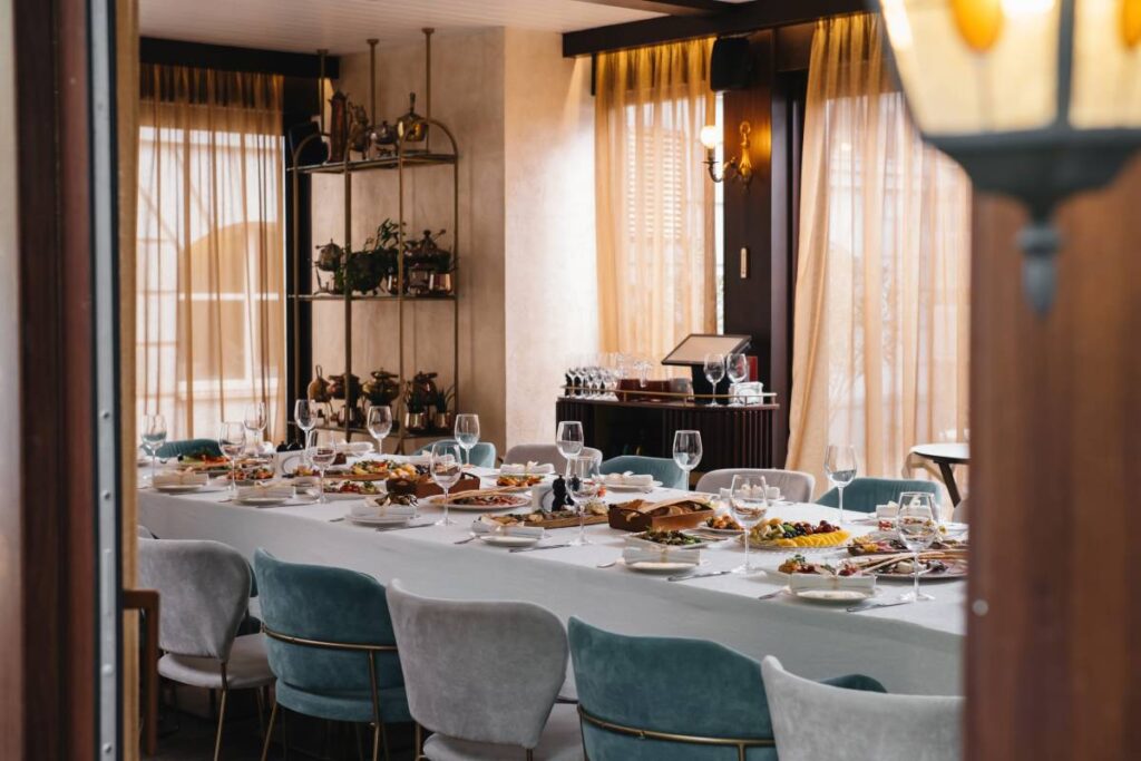 Long table before celebration in restaurant, empty glasses and appetizers, beg terrace windows. Cozy elegant atmosphere in luxury restaurant (Long table before celebration in restaurant, empty glasses and appetizers, beg terrace windows. Cozy elegant