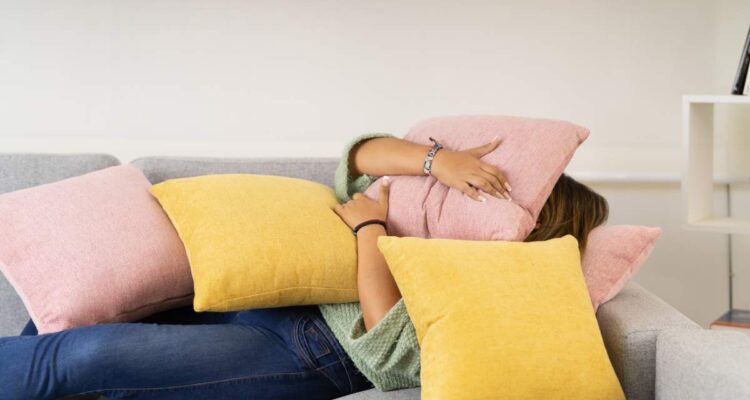 Horizontal photo of a sad woman among pillows lying on the sofa