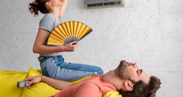 lying man with closed eyes and woman with hand fan suffering from heat at home