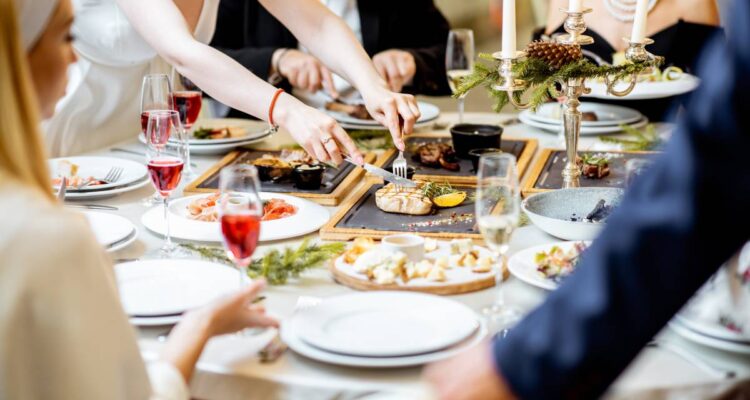 People having a festive dinner at a well-served table with tasty dishes during New Year Eve at the luxury restaurant, close-up view with no face